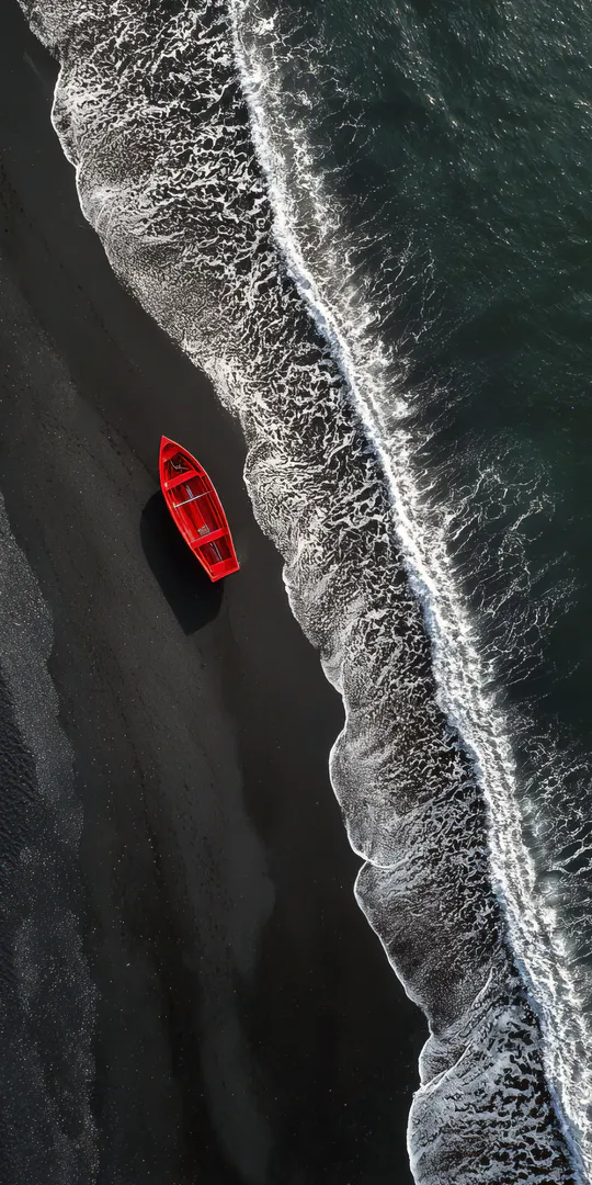 Phone wallpaper: Red boat on black sandy beach